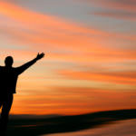 Man with outstretched arms facing a beautiful sunset.